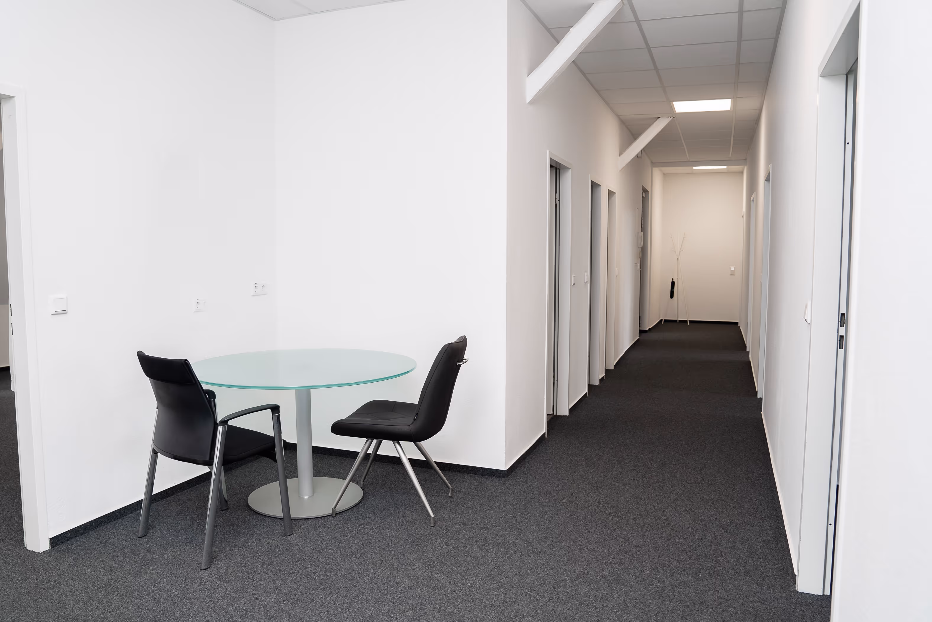 Heller Büroflur bei PG digital mit kleiner Sitzecke bestehend aus einem runden Glastisch und zwei schwarzen Stühlen – ideal für kurze Gespräche oder Pausen.