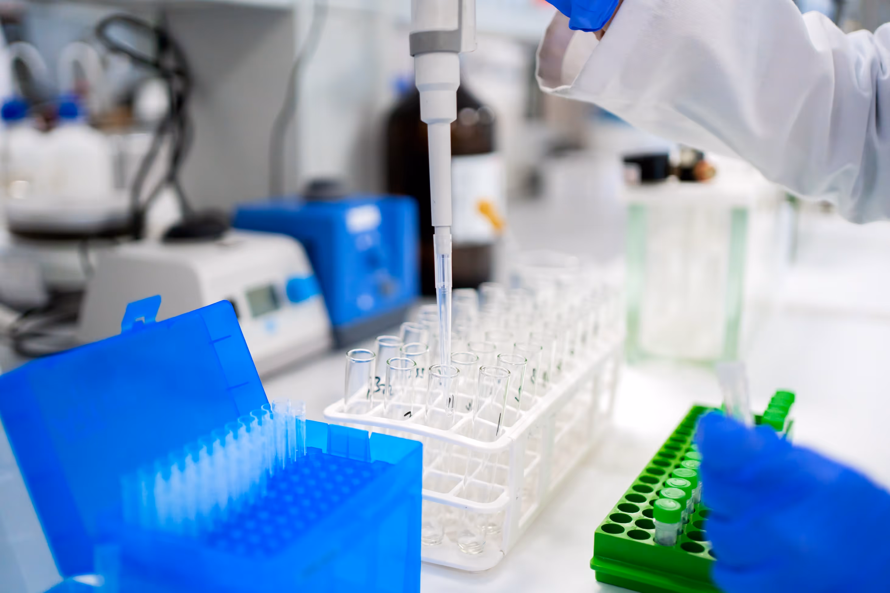 Laboratory scene showing a technician working under cGMP conditions, handling liquid samples and test tubes.