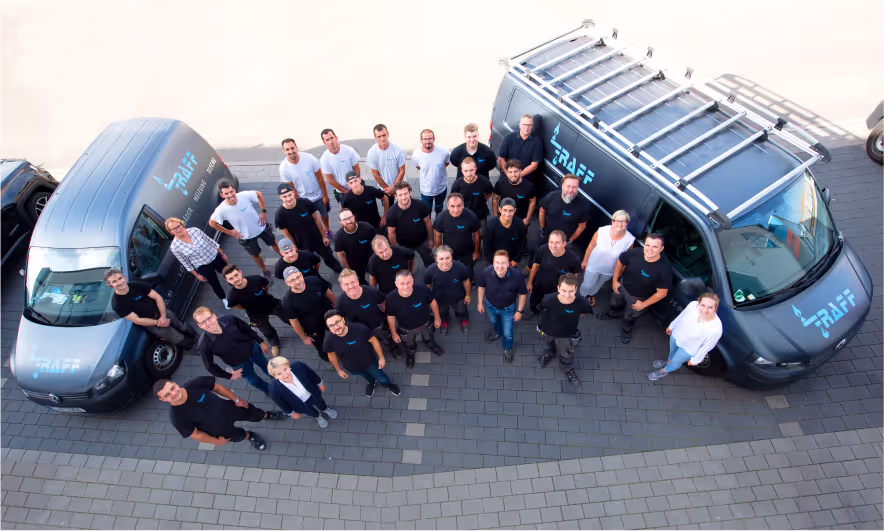 Teamfoto vor Firmenfahrzeugen auf dem Hof.