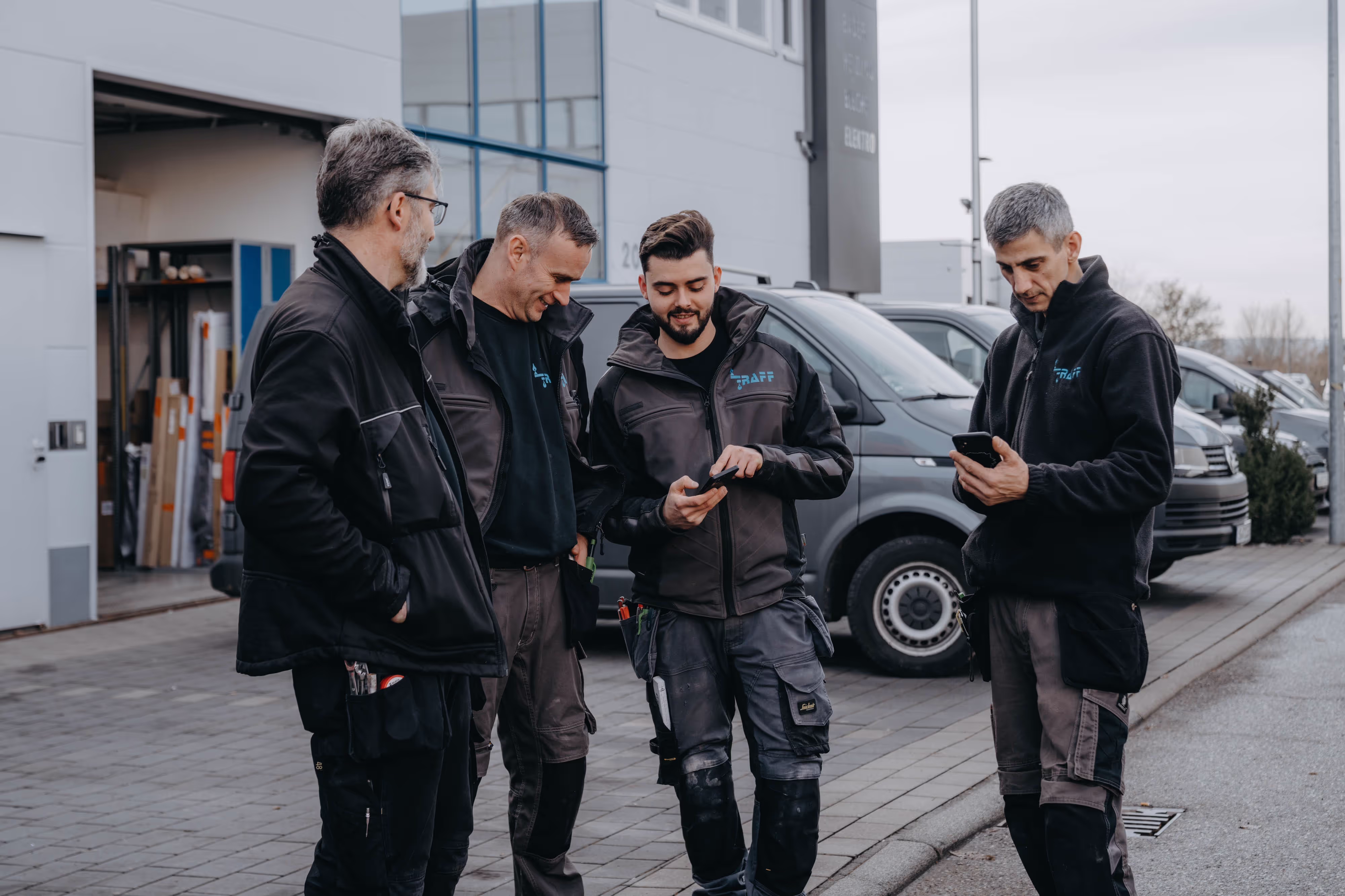 Vier Handwerker besprechen sich vor Firmenfahrzeugen.