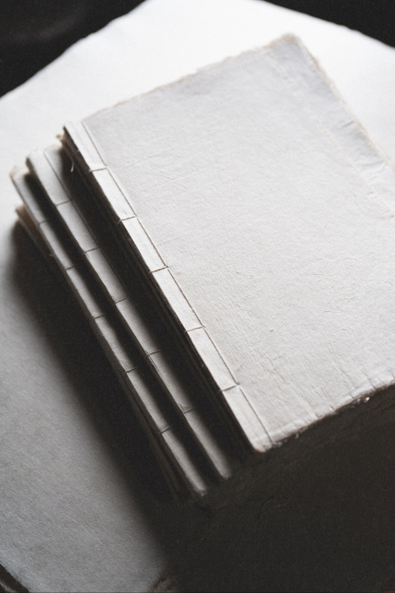 Stack of small handmade journals with varied natural paper textures in old world setting with fine art paper texture overlay.
