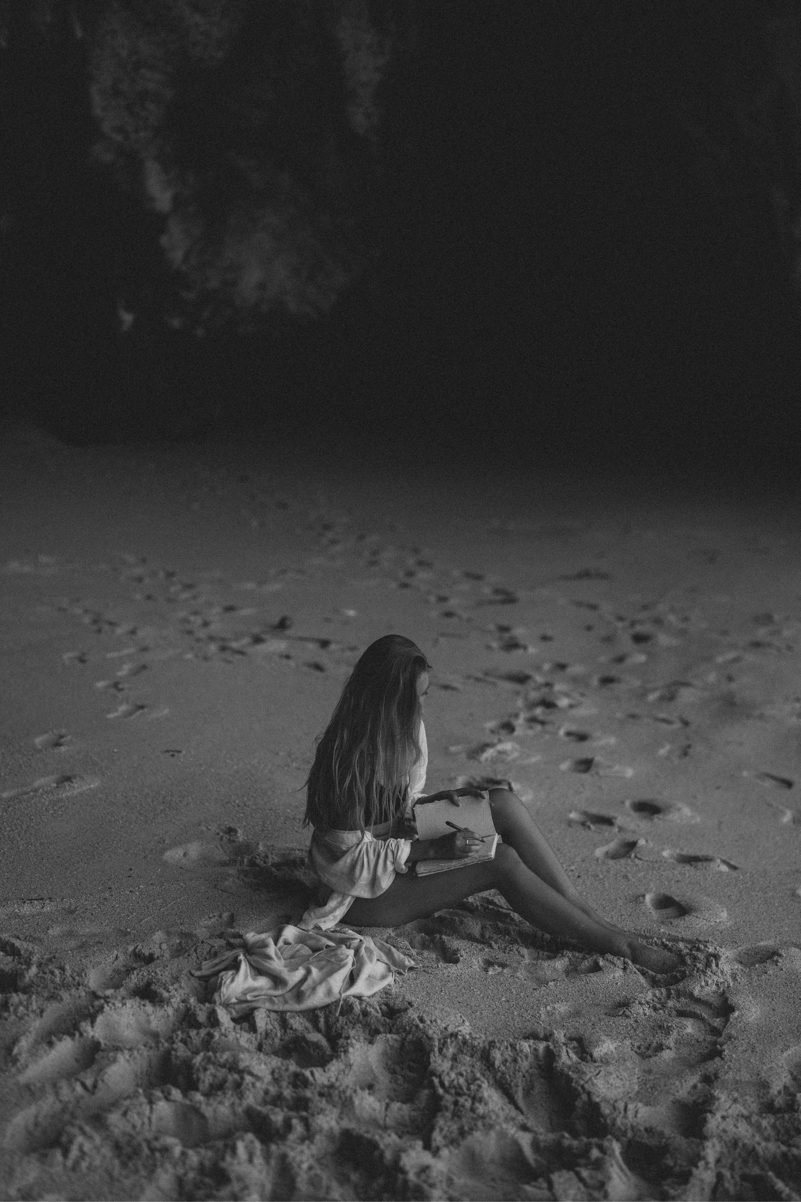 Woman on the beach pausing in thought with natural fiber journal in hand, black-and-white photography