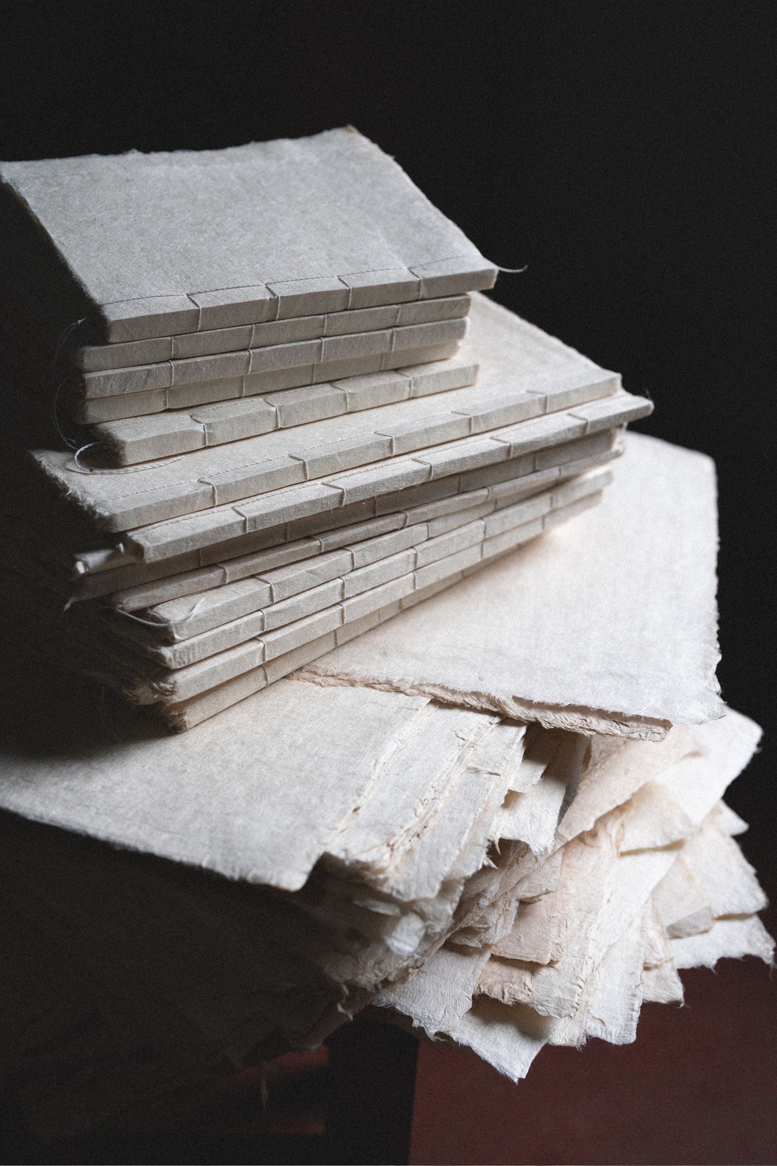 Close-up shot of stack of small handmade journals with varied natural paper textures in old world setting with fine art paper texture overlay.