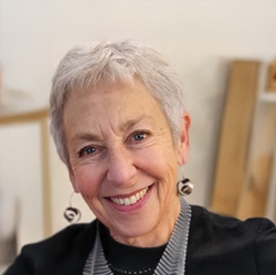 Headshot of a woman with short light hair and a black top in a white room