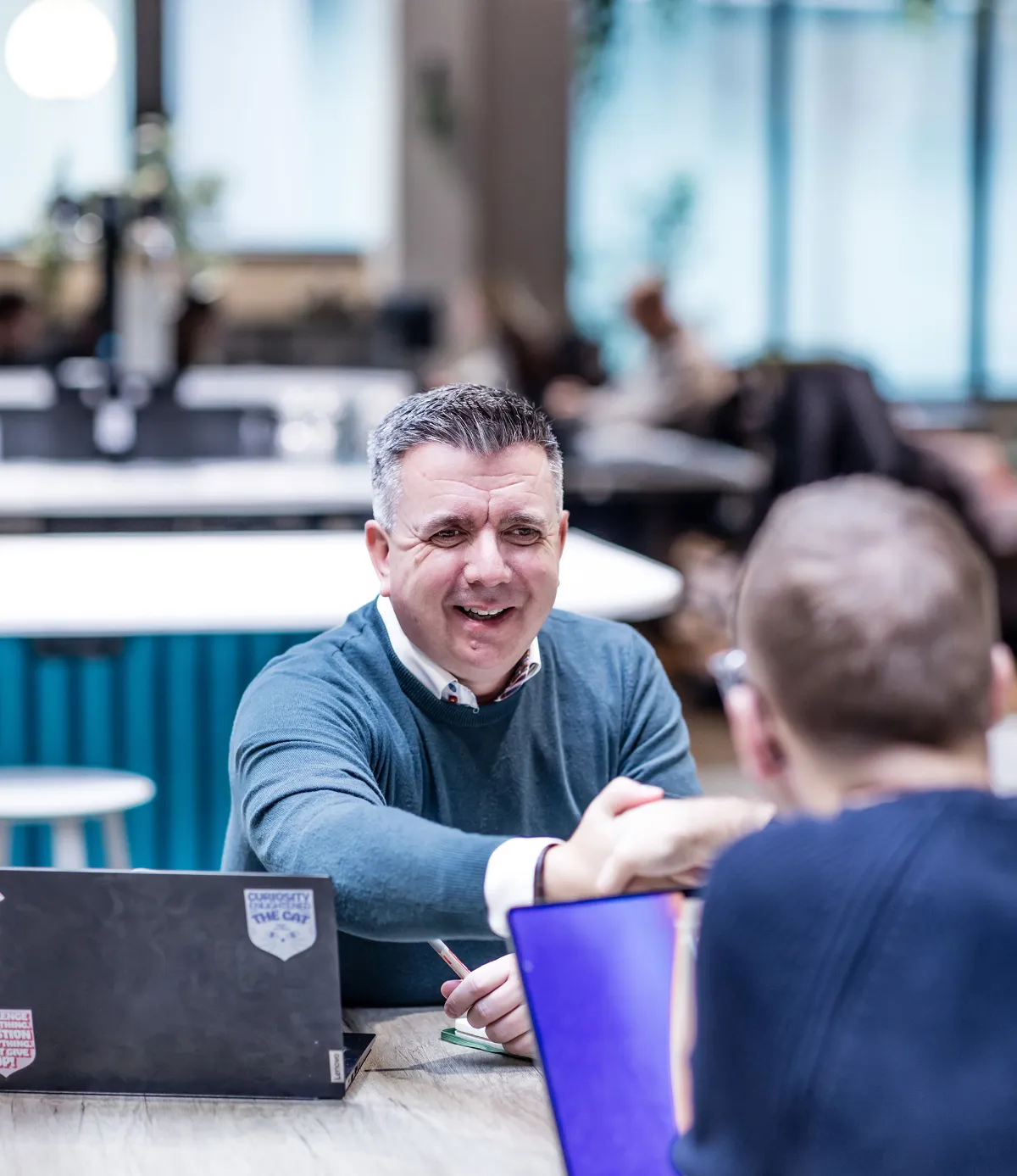 Consultant shaking hand with a client over a laptop in a large trendy office