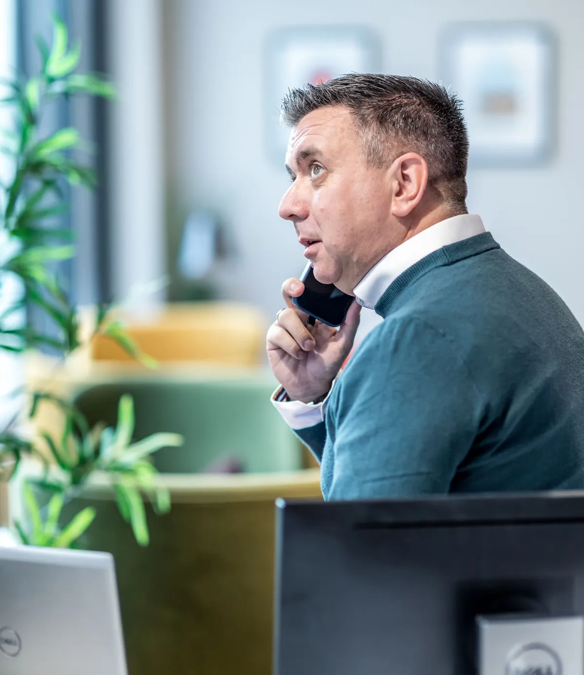 Man in a white shirt and blue sweatshirt on a call with his mobile phone.