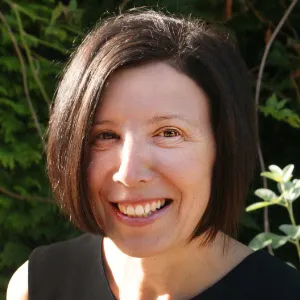 Profile shot of woman with short dark brown hair smiling outside.