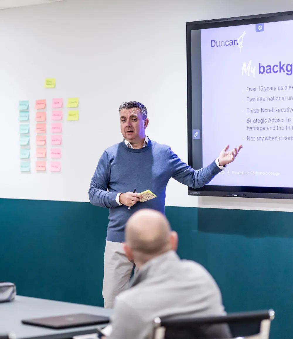 People sitting around a conference table with a consultant who is presenting a slideshow..