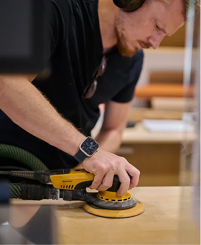 Un homme utilise une ponceuse électrique ronde sur une surface en bois dans un atelier.