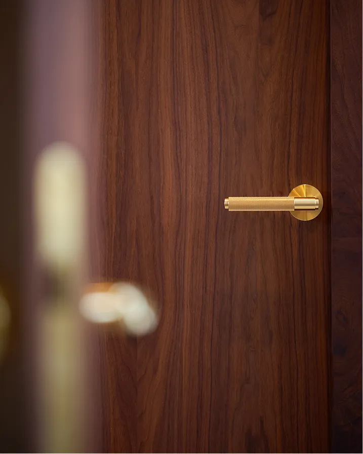 Poignée de porte dorée fixée sur une porte en bois foncé avec un motif de grain apparent.