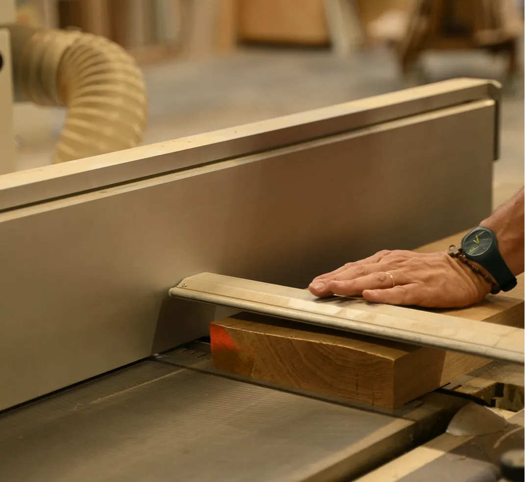 Main d'un artisan guidant une planche de bois sur une raboteuse dans un atelier de menuiserie.
