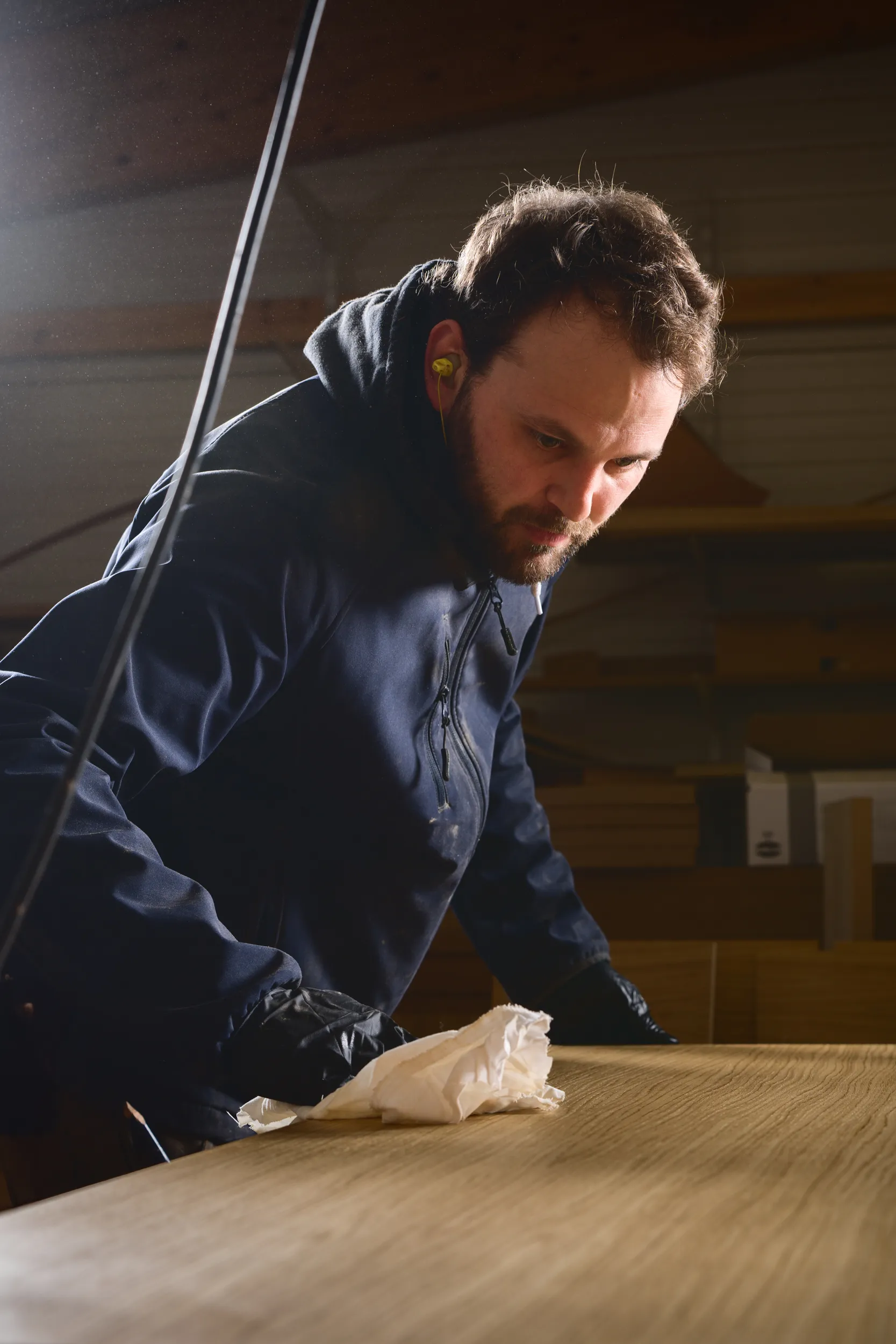 Un homme portant un sweat à capuche et des gants nettoie une surface en bois avec un chiffon.