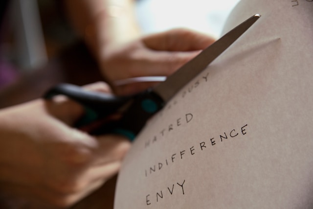 Person cutting paper with the words jealousy, envy, indifference and hatred. 