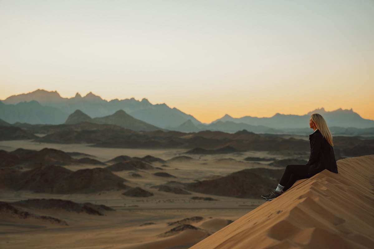 Woman sitting on sand dunes looking into the distance