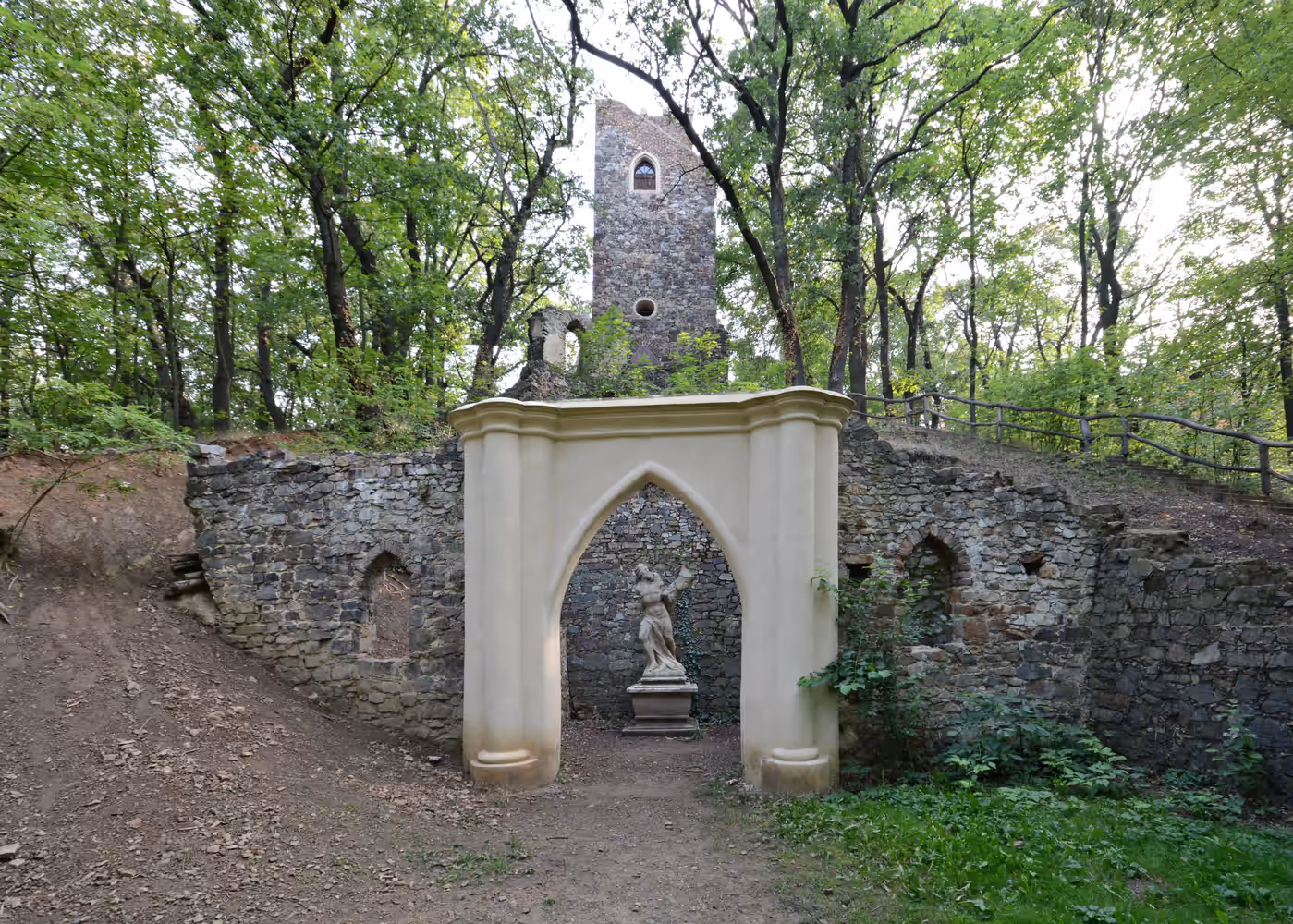 Stone ruins of a tower and wall in a forest with a beige archway featuring a classical statue inside.