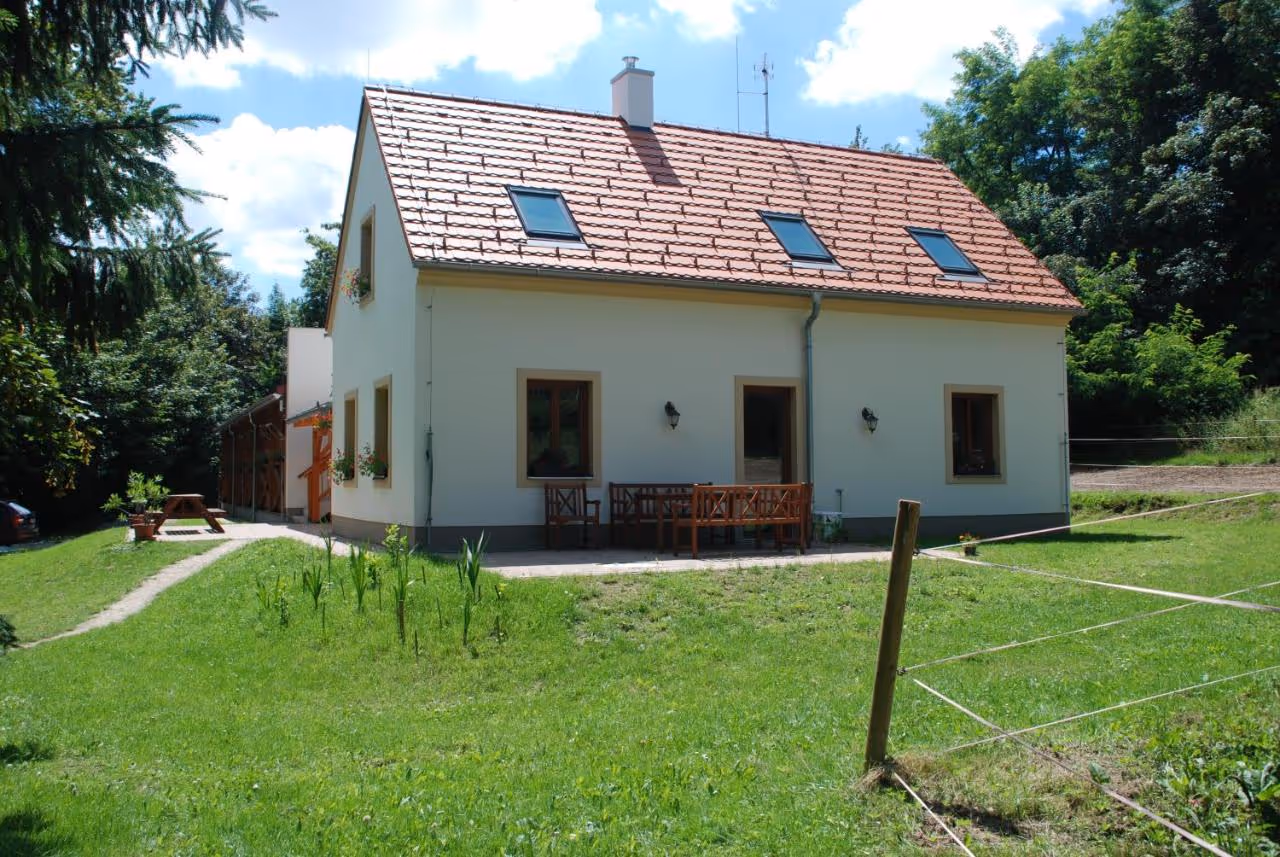 White two-story house with terracotta roof and three skylights surrounded by green lawn and trees on a sunny day.