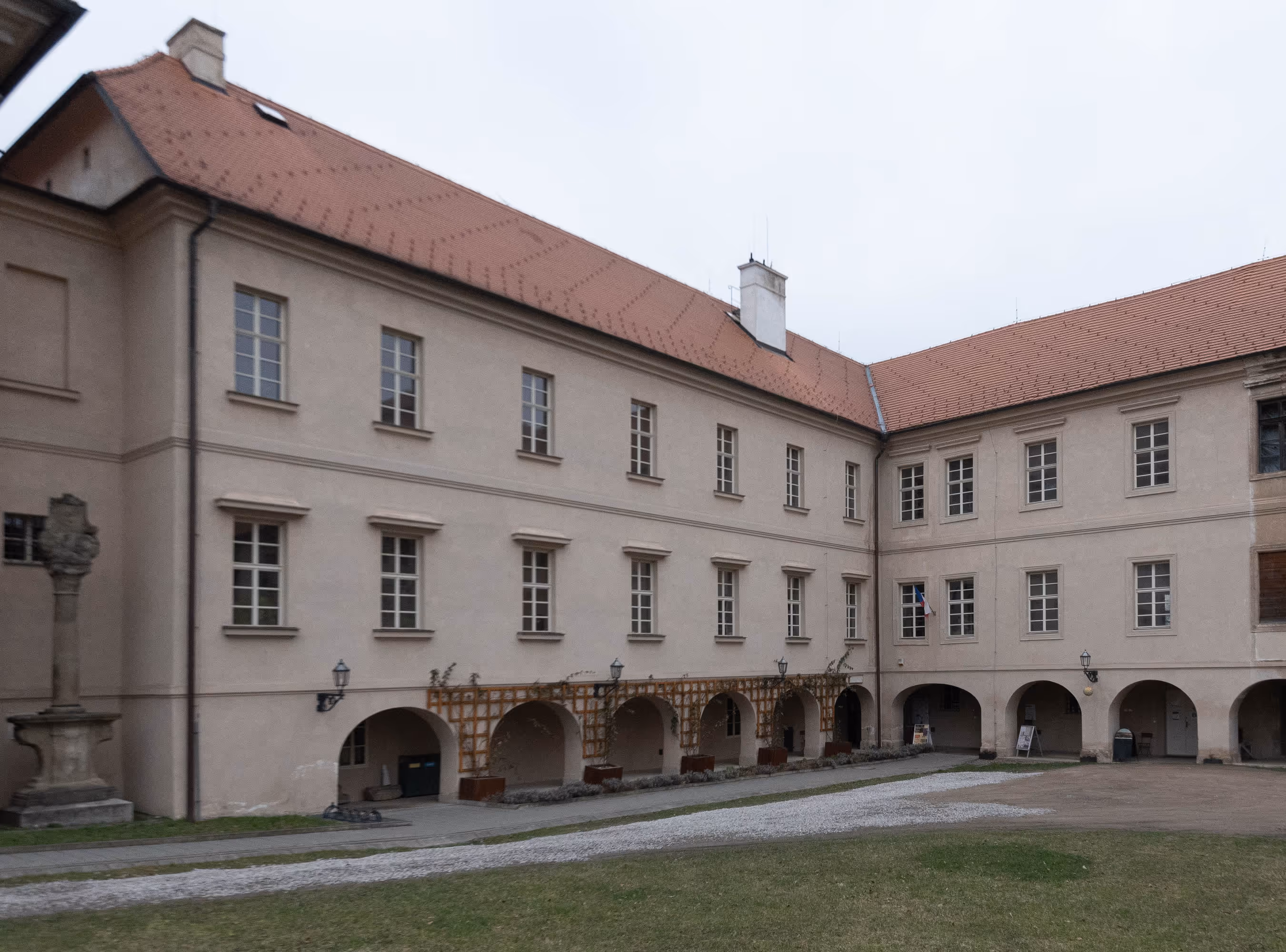 Historic beige building with red-tiled roof and multiple windows surrounding a courtyard with grass and a stone path.