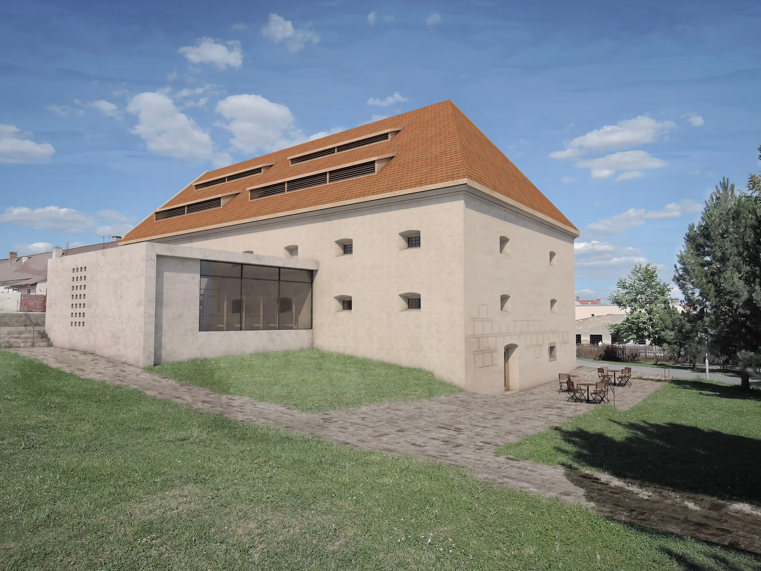 Modern building with beige walls and a red-tiled roof, featuring a large glass window extension and outdoor seating on a paved area surrounded by grass.