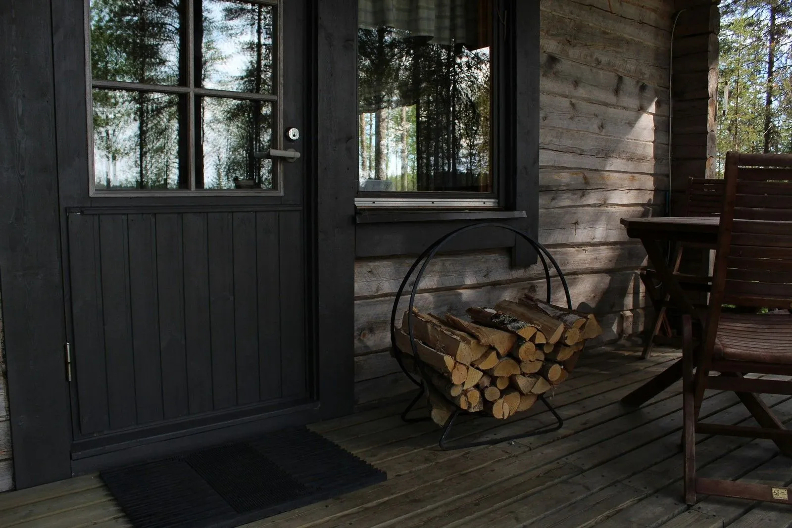 A cozy cabin entrance featuring a wooden door, a pile of logs in a decorative holder, and a rustic wooden table set on the porch.
