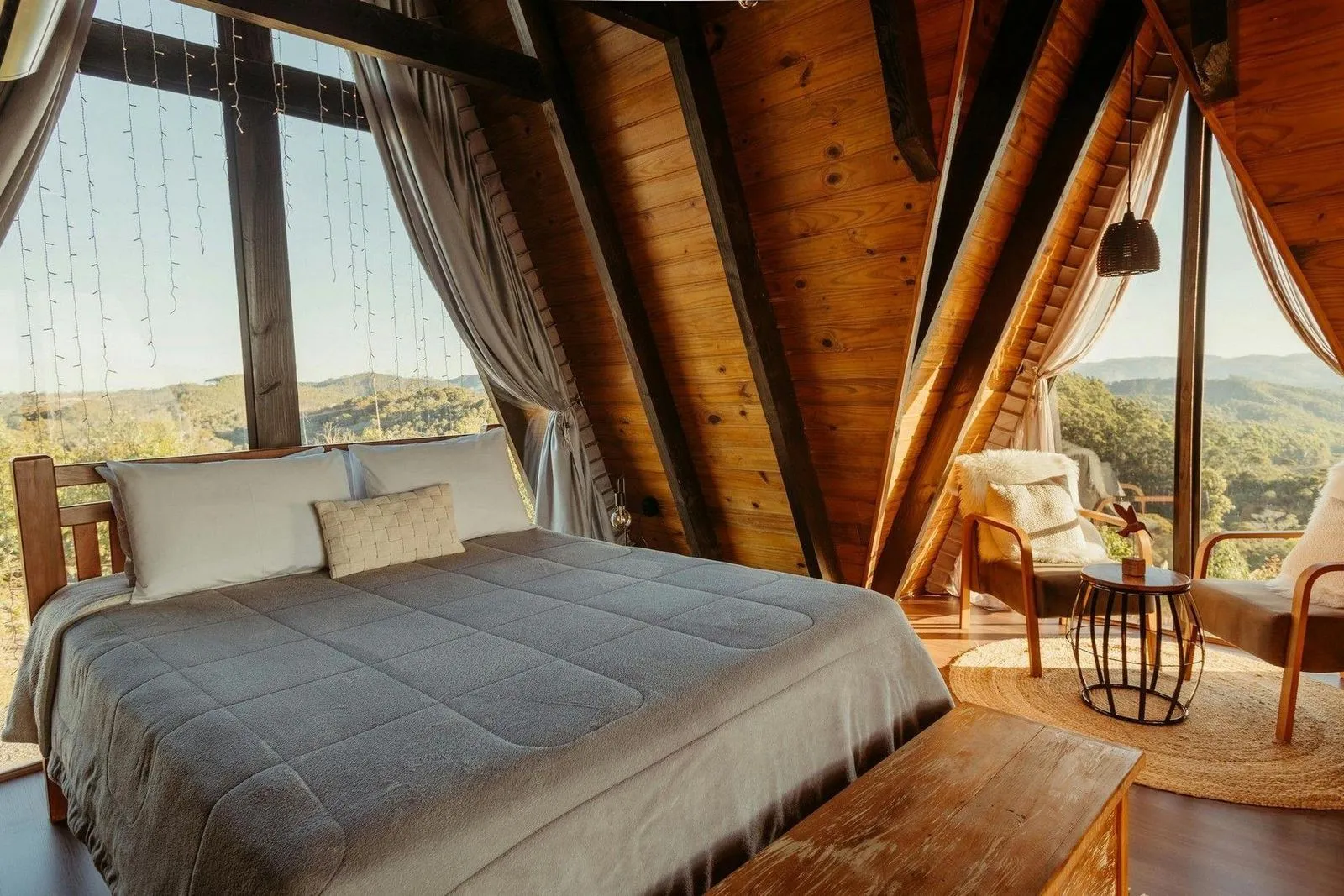 Cozy A-frame bedroom with wooden decor, a comfortable bed, and floor-to-ceiling windows showcasing a scenic mountain view.
