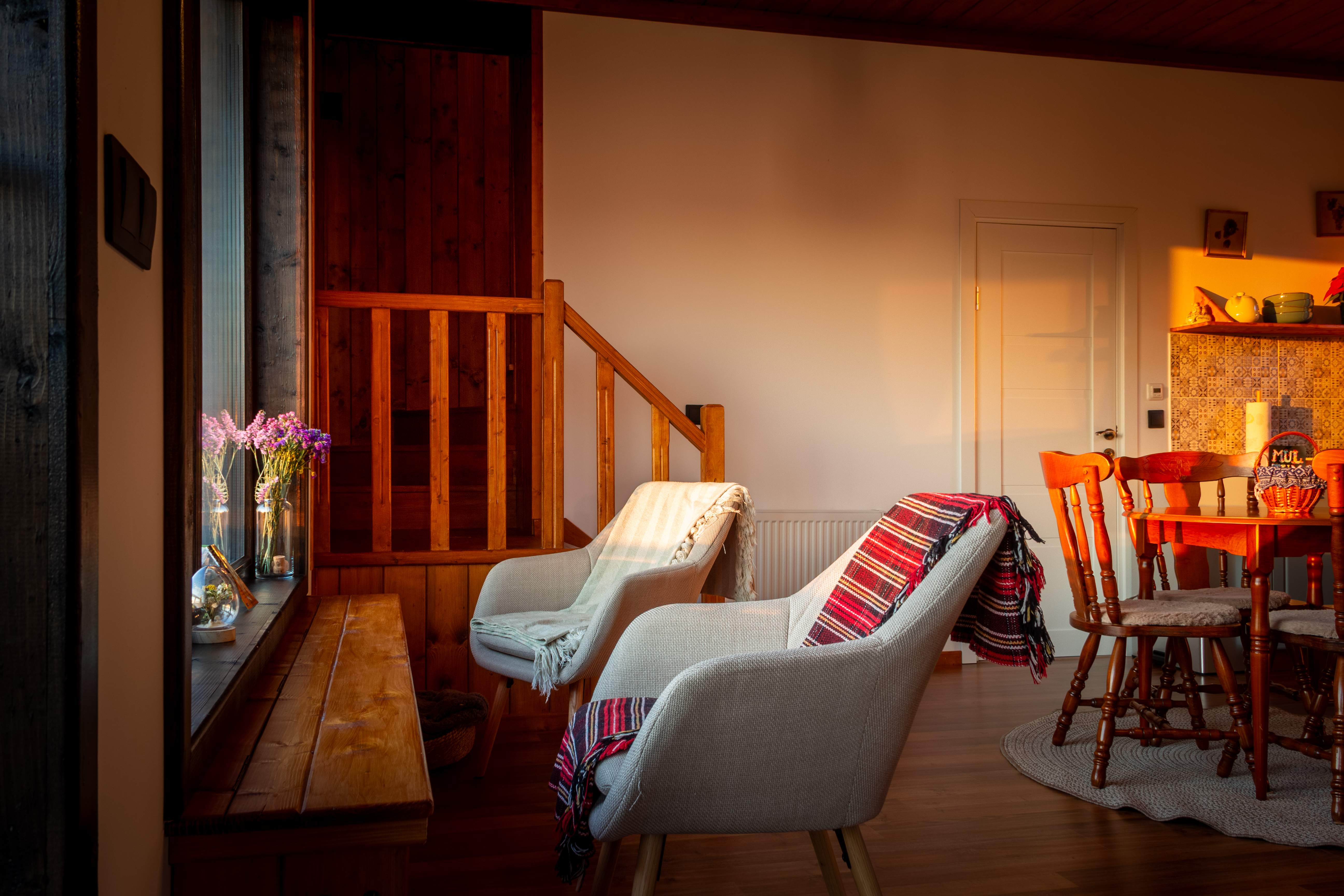 Cozy living room corner with a light gray couch adorned with decorative pillows, natural light filtering through windows, and potted plants.