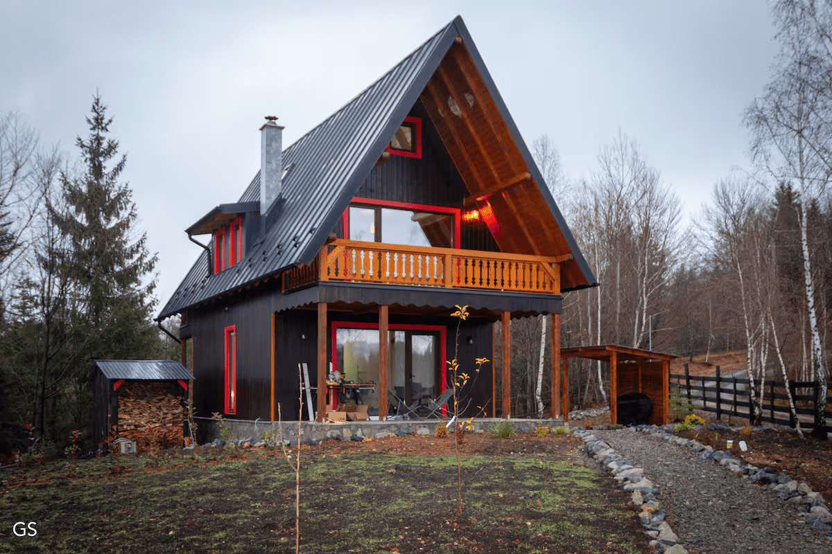 Cozy cabin nestled among lush green trees, with a clear blue sky and distant hills visible in the backdrop.