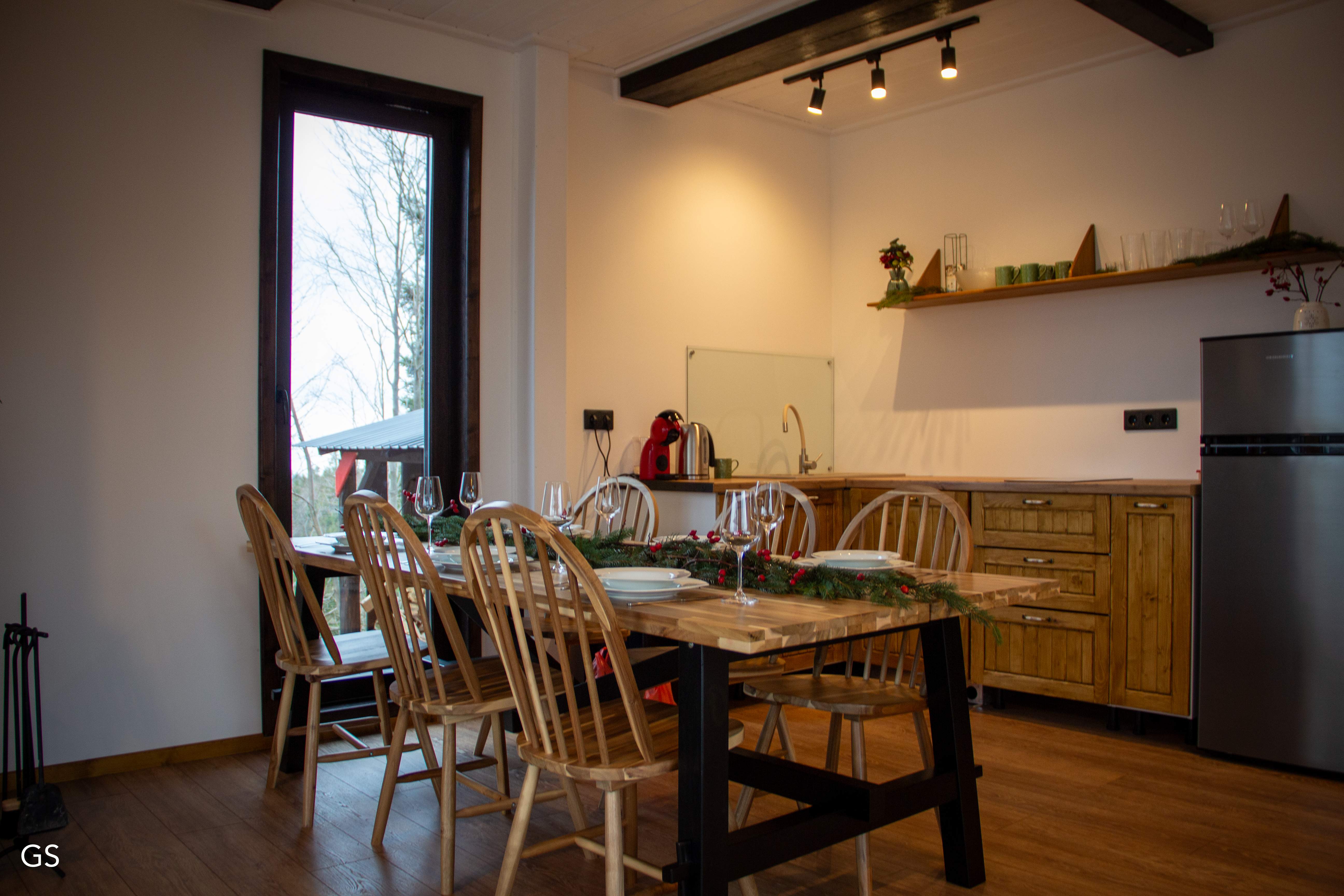 A modern mountain house nestled among lush green trees and hills under a cloudy sky, surrounded by tranquil nature.