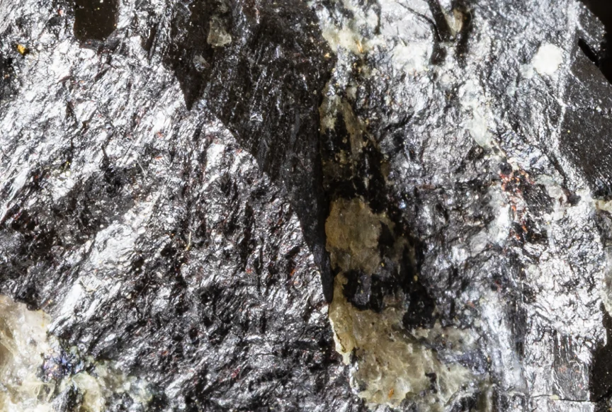Close-up of a metallic, shiny black mineral rock with silver and beige patches.