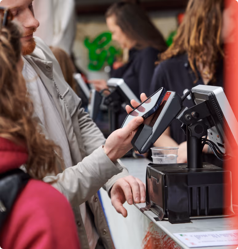 A close-up of a person making a contactless payment with their smartphone at a festival bar.