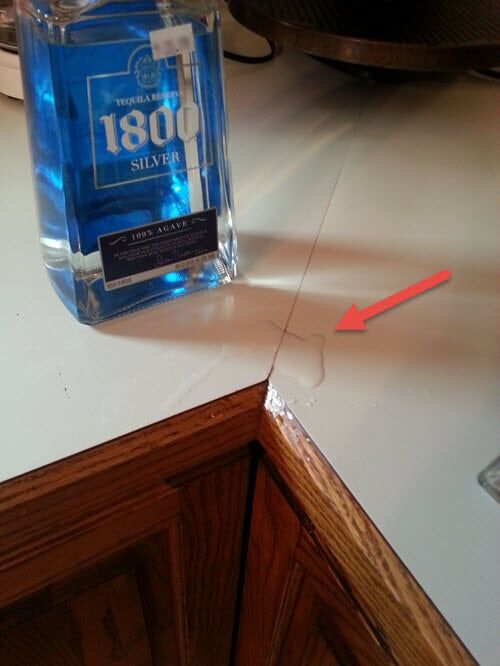 Small puddle of spilled tequila on a counter with the bottle of 1800 Silver Tequila next to it
