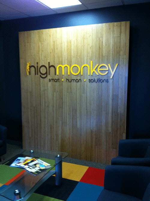 High Monkey Logo on a wood-paneled wall in a sitting area with chairs and coffee table