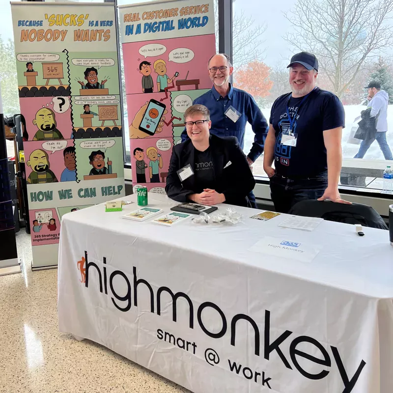 Three High Monkey employees behind a table at their booth, two comic graphics behind them