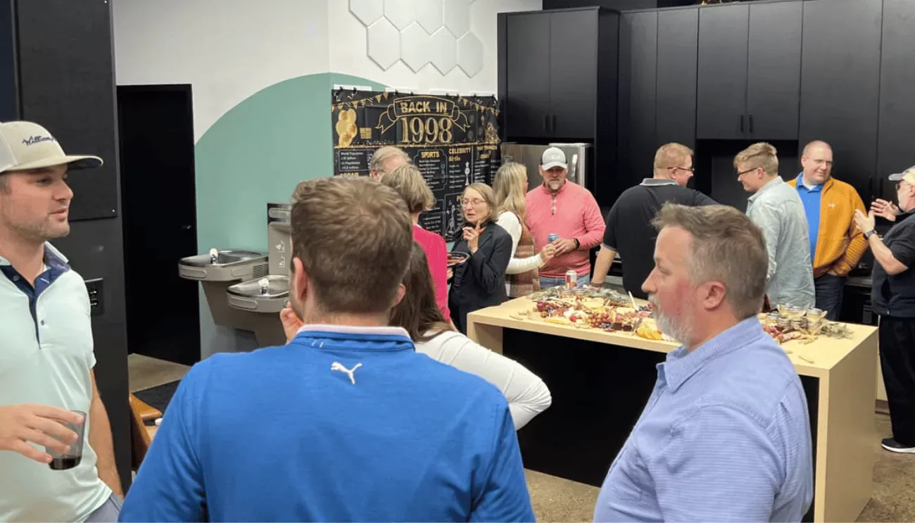 A casual office celebration with people gathered around a snack table, marking High Monkey’s 25-year anniversary.