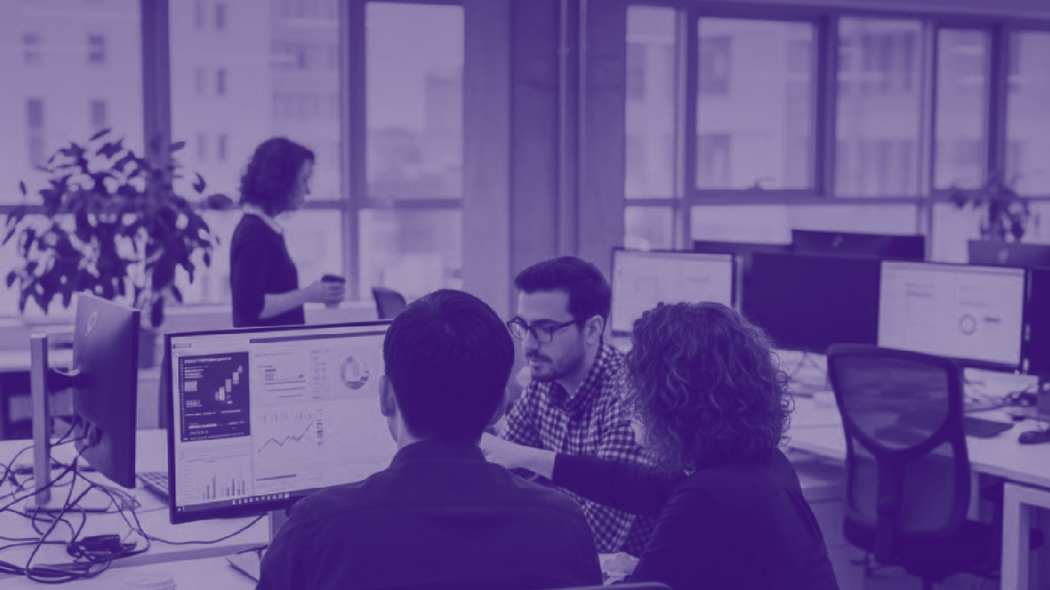 Un team di colleghi lavora insieme in ufficio davanti a monitor con dashboard e grafici, confrontandosi su dati e analisi.