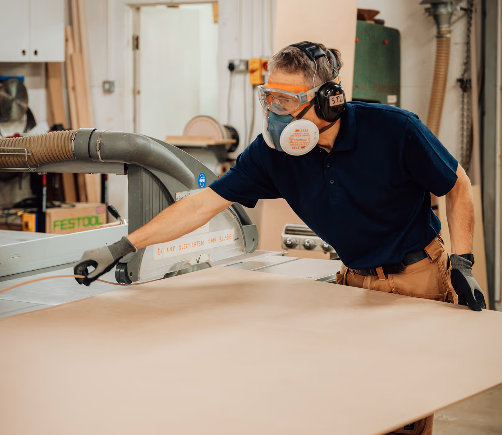 A man wearing a mask and safety goggles is working on a piece of wood.