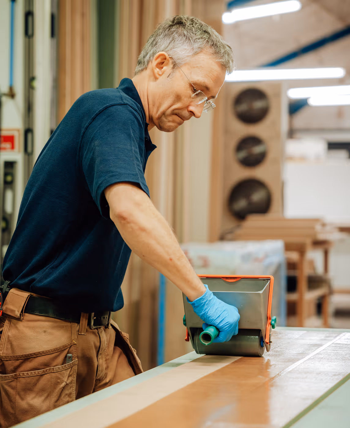 A man wearing a blue shirt and blue gloves is working on a wooden table.