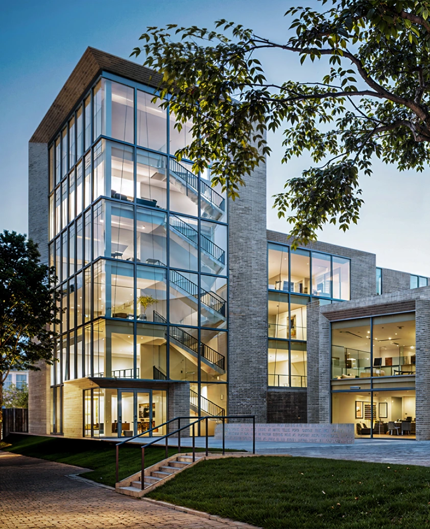Radiance Visual. Modern multi-story office building with large glass windows showcasing staircases and interior lighting at dusk.
