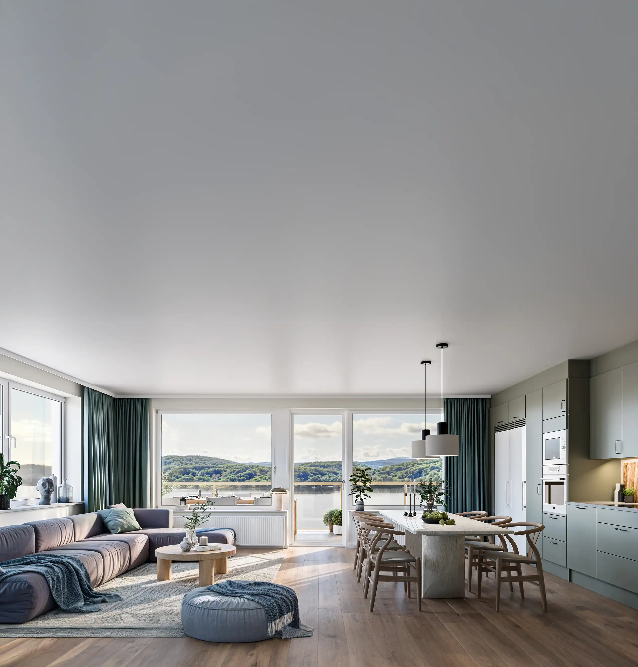 Radiance Visual. Modern open-plan living room and kitchen with large windows overlooking a lake and green hills, featuring a gray sectional sofa, round coffee table, dining table with wooden chairs, and green cabinetry.