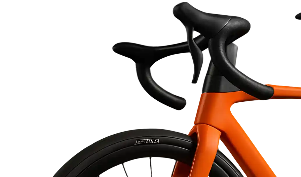 Radiance Visual. Close-up of an orange road bike's front fork, black handlebar, and front wheel with a black tire.