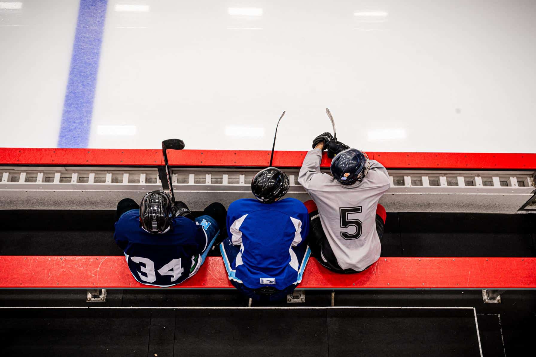 Three hockey players sitting on the bench in full gear, watching the game from the sidelines.