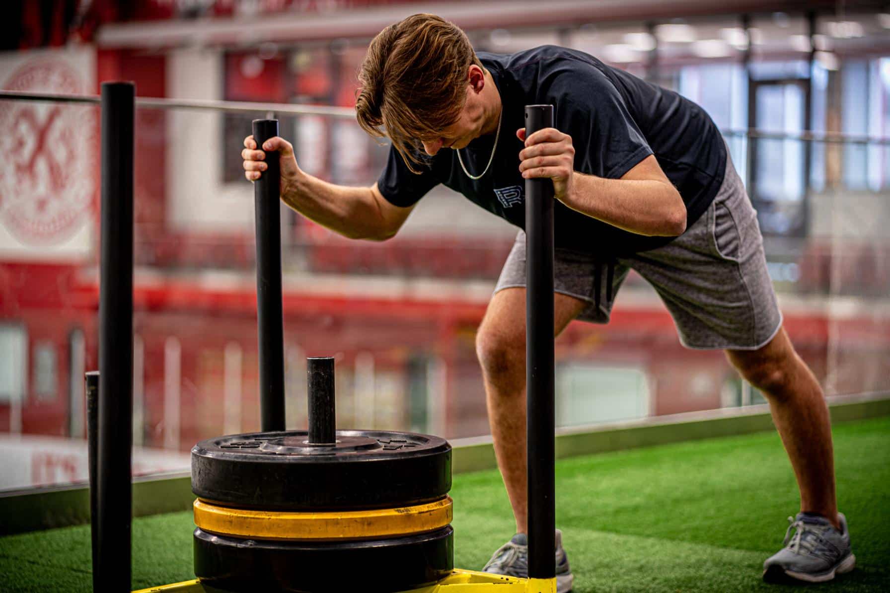 Athlete pushing a weighted sled on indoor turf during strength and conditioning training.