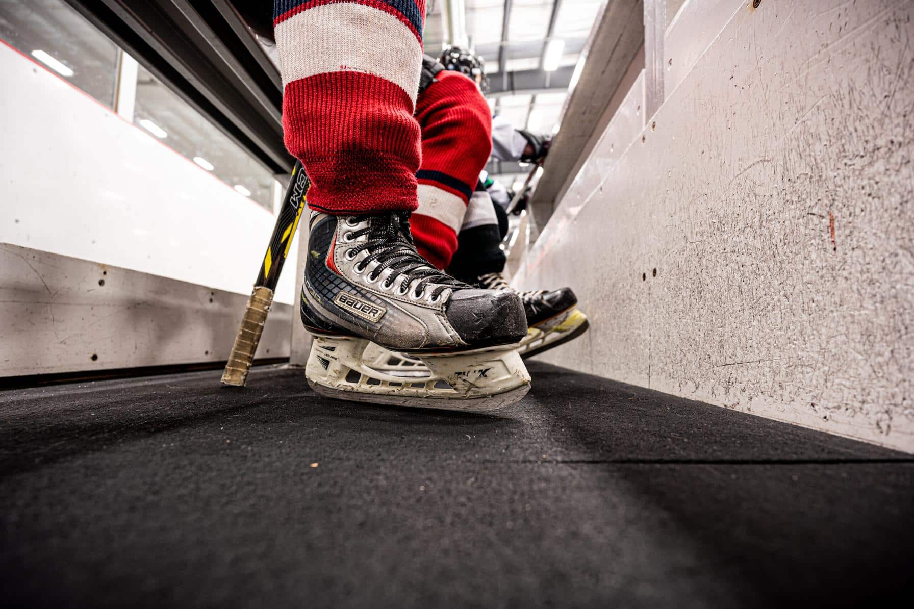 Close-up of a hockey player’s skates and stick near the bench area during a game.