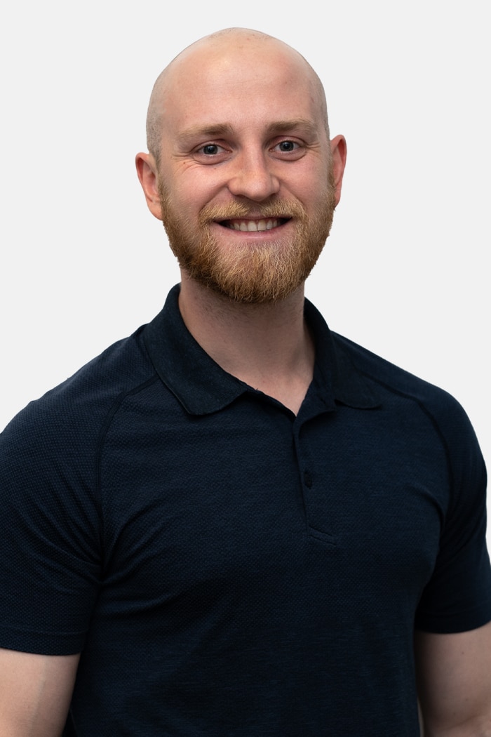Smiling bald man with a reddish beard wearing a dark navy polo shirt, photographed against a plain light gray background.