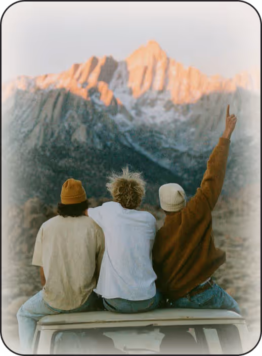 Three people sitting on top of a car looking at the mountains.