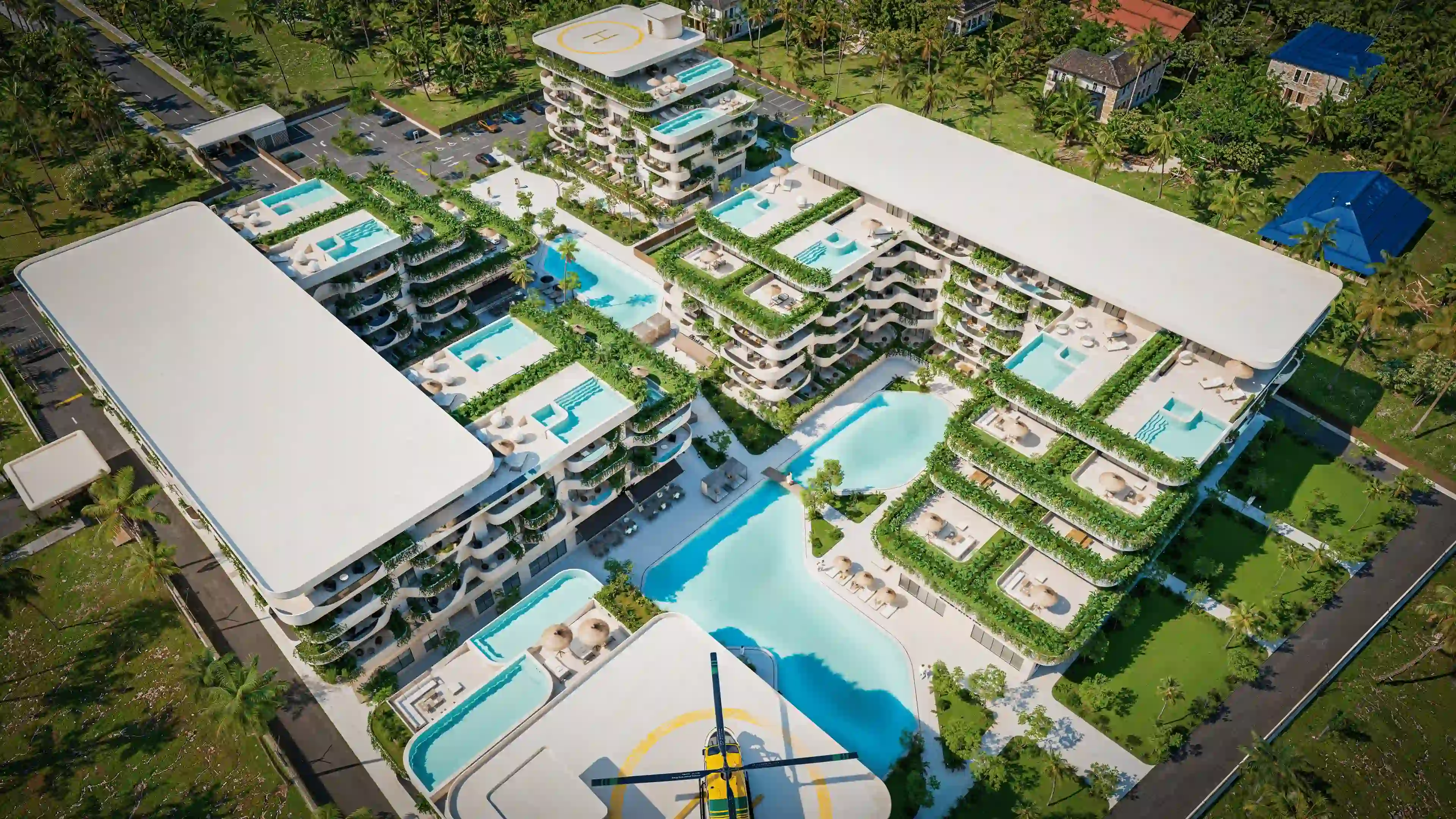 Aerial view of a modern luxury resort with multiple buildings featuring rooftop pools, green terraces, a large swimming pool at the center, and a helicopter on a helipad.