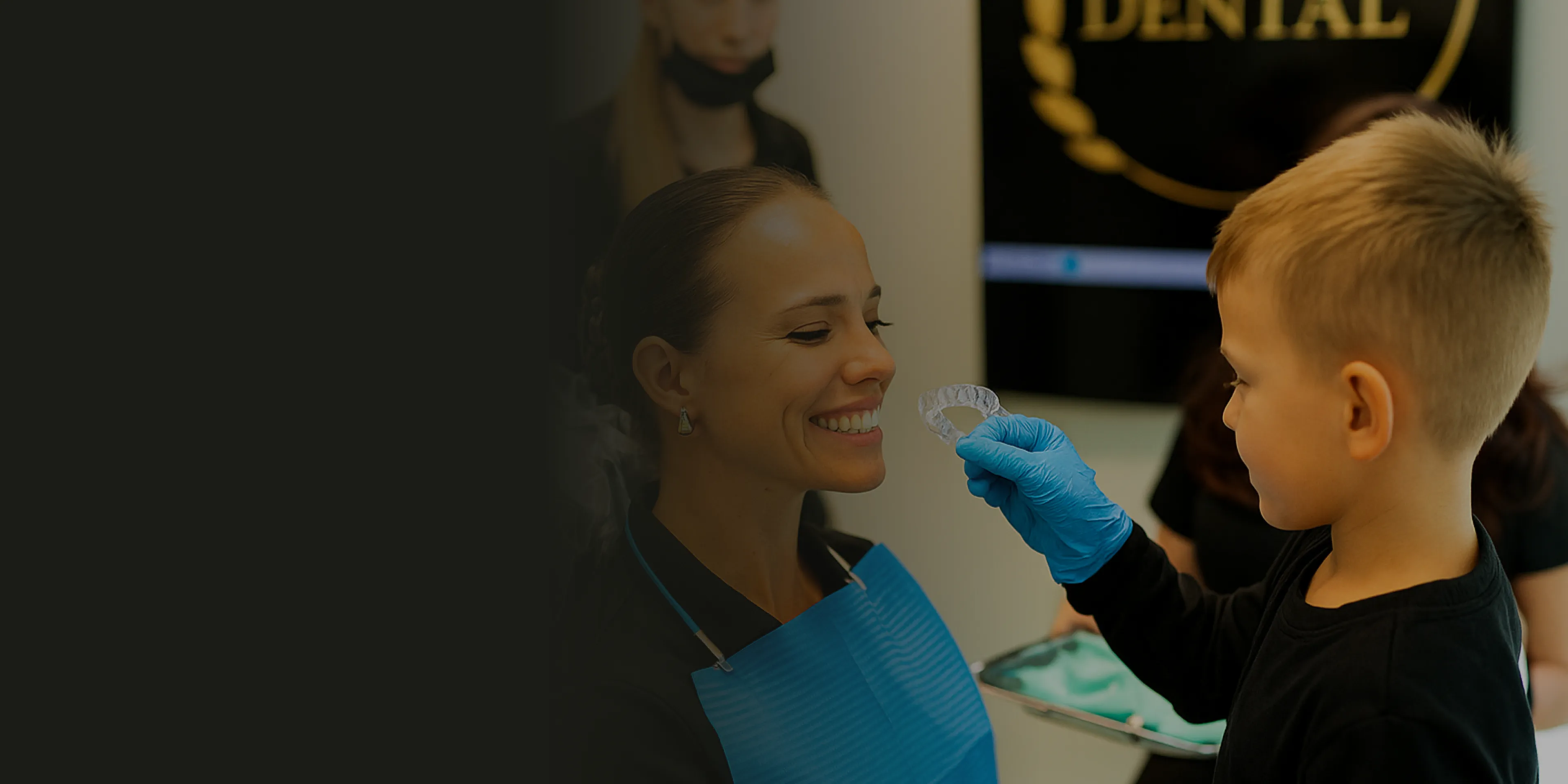 A child in gloves holds a dental aligner for a smiling woman in a dental office.
