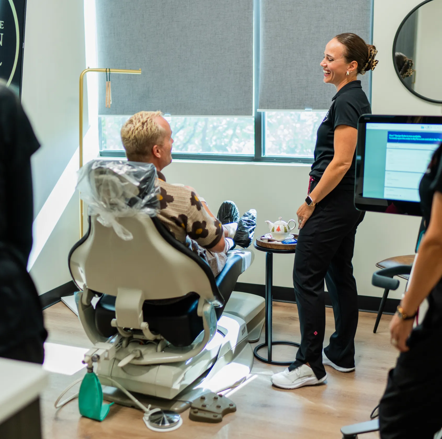 A person sits in a dentist chair while a dental hygienist smiles and talks to them.