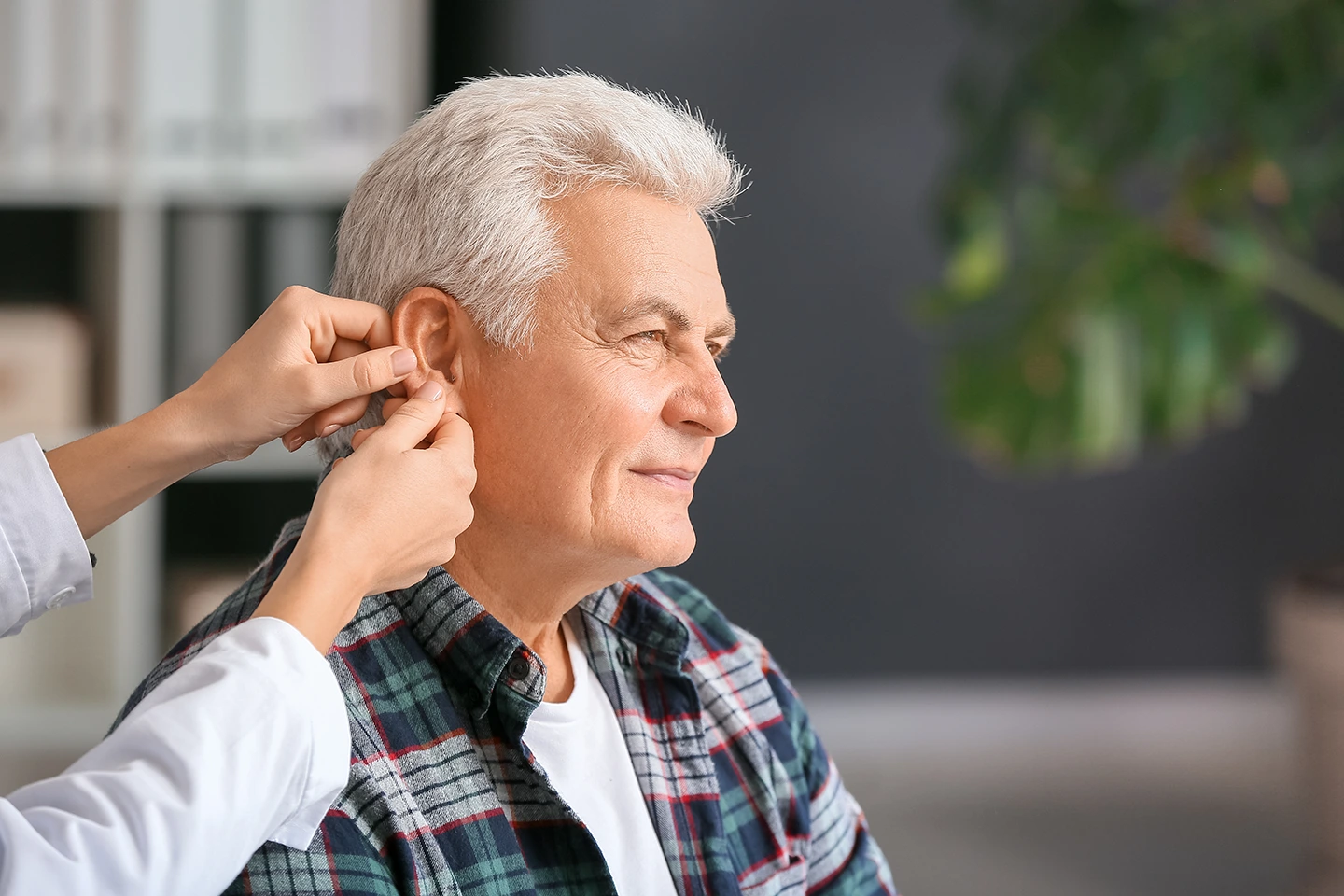 Senior man receiving hearing aid fitting from a healthcare professional in a clinical setting.