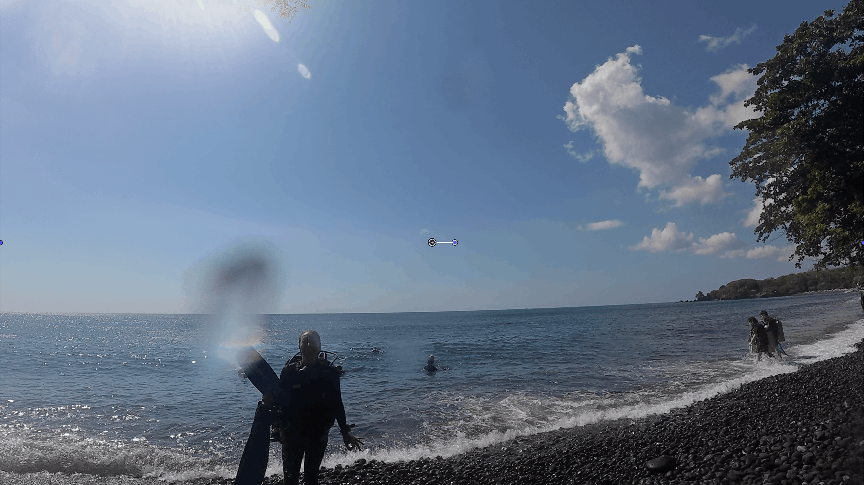 Diver walking into the water at a black sand beach shore entry with other divers wading in behind