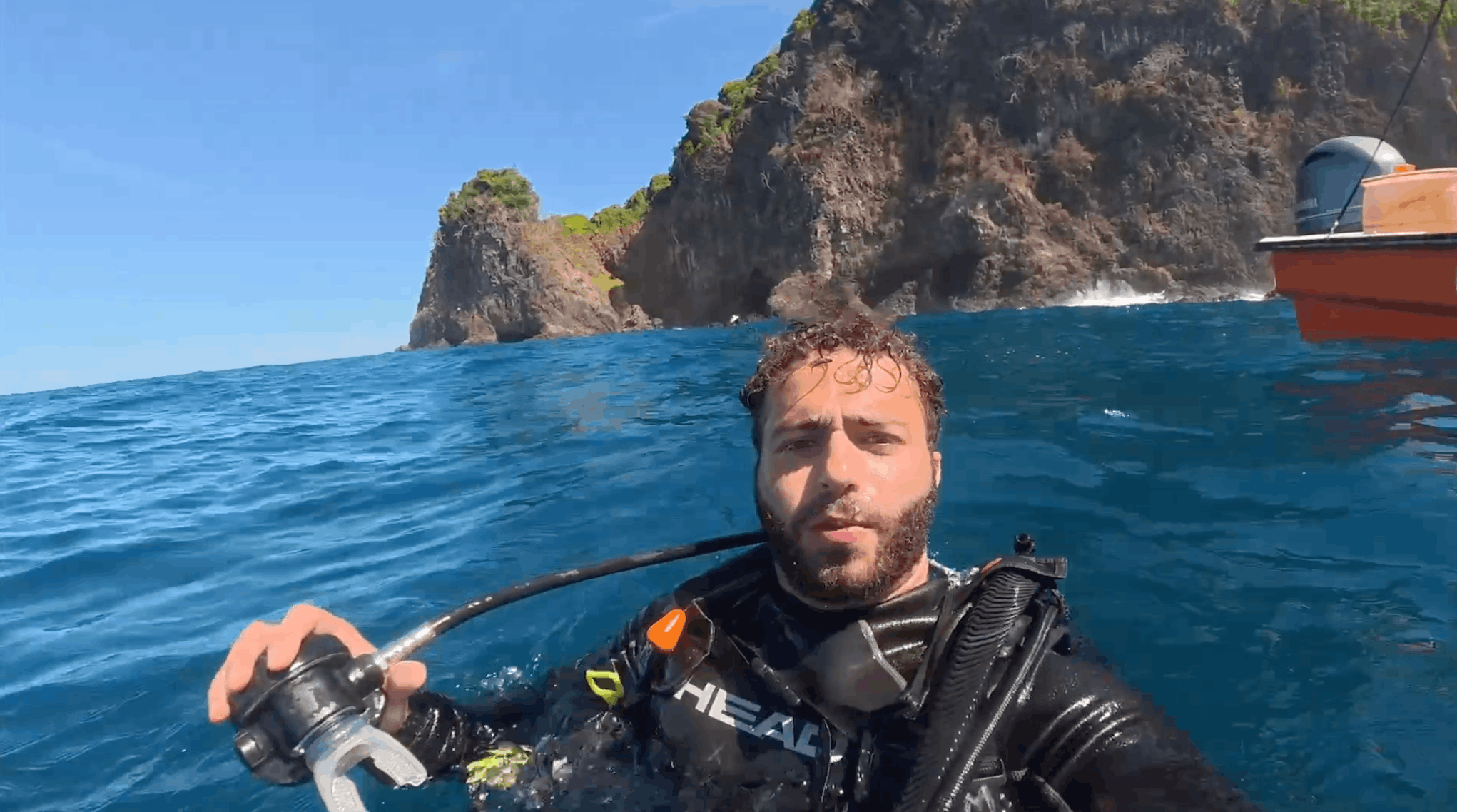 Austin at the surface in scuba gear holding his regulator with a rocky islet behind him, Coiba 🇵🇦